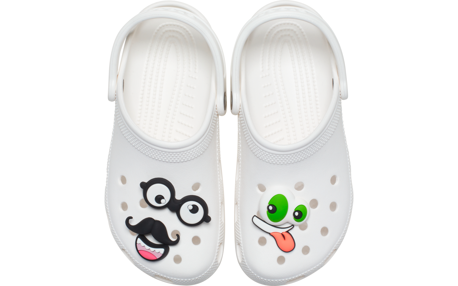 Par de zuecos blancos visto desde arriba. Zueco izquierdo con aplicaciones enganchadas: gafas negras y bigote, y aplicación de boca rosa. Zueco derecho con aplicación de ojo verde y aplicación de lengua fuera
