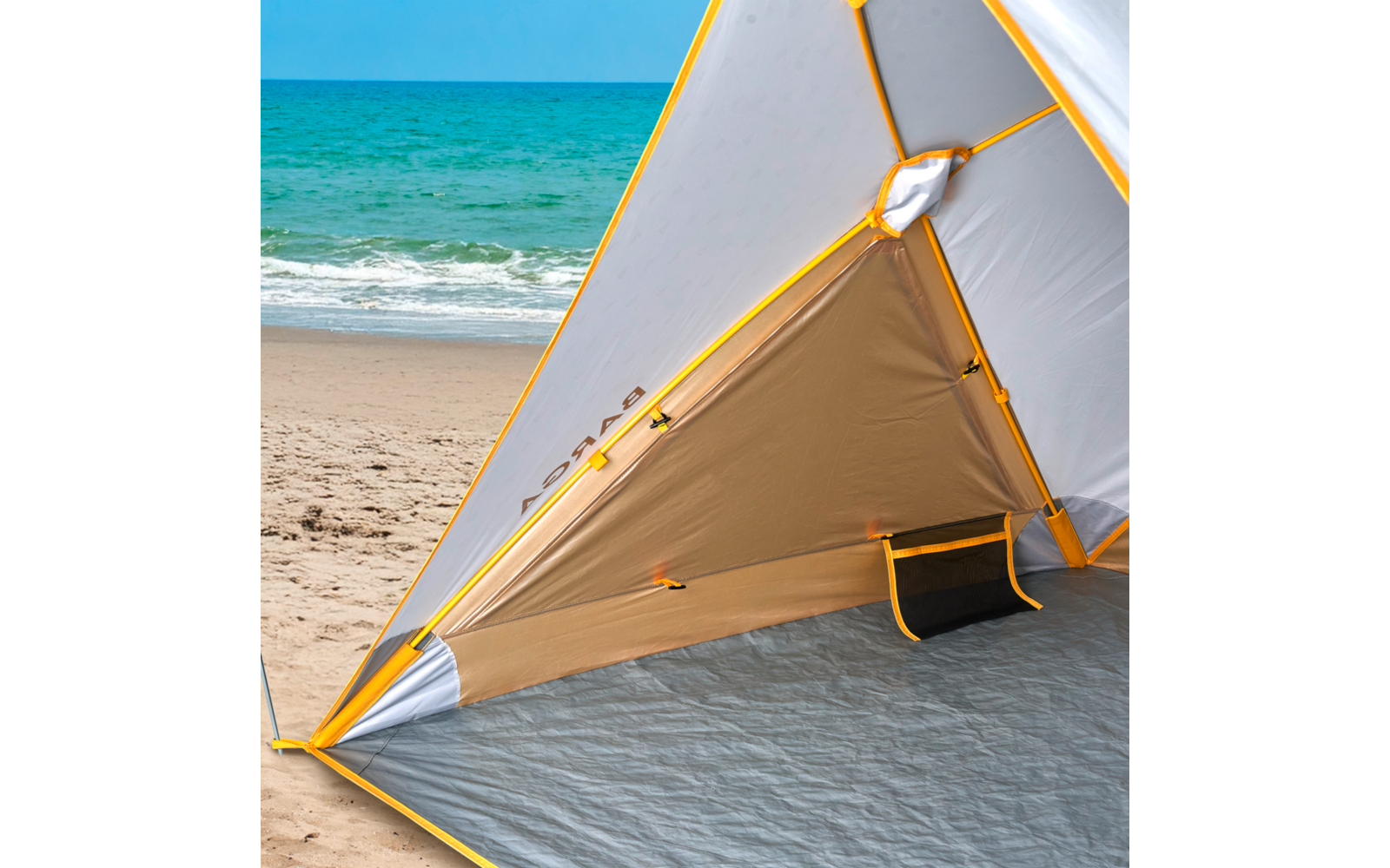 Innenansicht eines dreieckigen Strandzelts mit gelben Kanten und grauer Bodenmatte; im Hintergrund Sandstrand und türkisfarbenes Meer mit kleinen Wellen