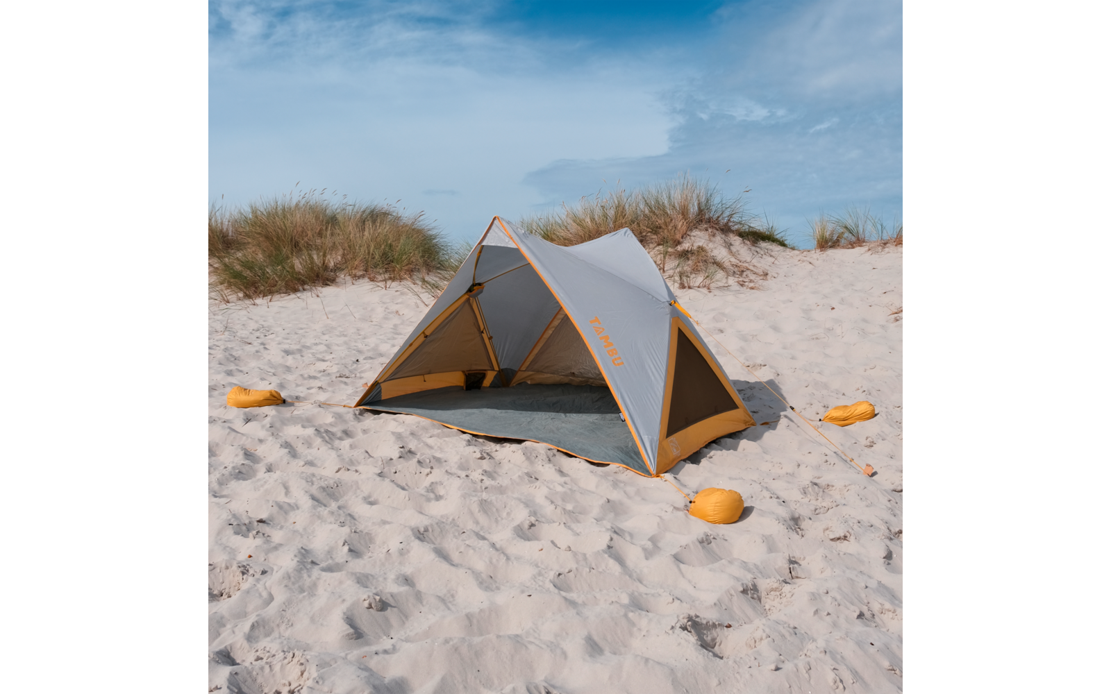 Graues und orangefarbenes Zelt auf weißem Sandstrand, im Hintergrund Sanddünen mit Strandgras und blauer Himmel