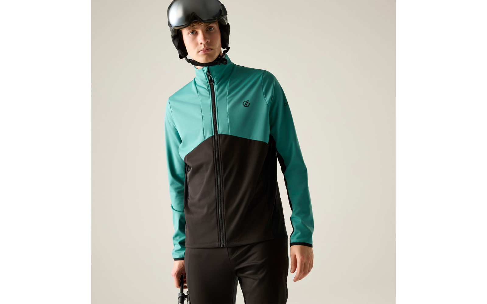 Person mit schwarzem Skihelm, türkis-schwarzer Jacke und schwarzen Hosen vor hellem Hintergrund