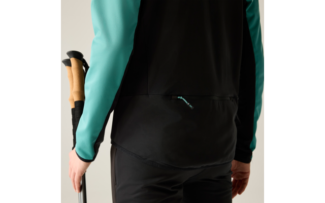 Rückenansicht einer Person von der Taille abwärts, schwarzes Vest mit türkisfarbenen Ärmeln, hält zwei Wanderstöcke mit Korkgriffen in der linken Hand