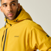 Nahaufnahme einer Person in gelber Kapuzenjacke, Blick nach links, heller Hintergrund, kleines Logo auf der Brust