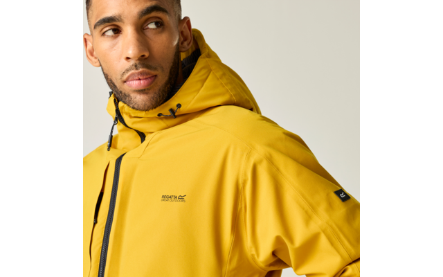 Nahaufnahme einer Person in gelber Kapuzenjacke, Blick nach links, heller Hintergrund, kleines Logo auf der Brust