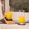Zwei Gläser mit Orangensaft auf einem Küchentresen, eines steht aufrecht, das andere ist auf einem schrägen Holzbrett geneigt