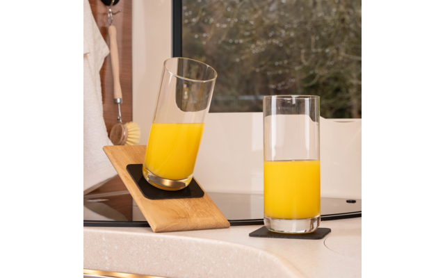 Zwei Gläser mit Orangensaft auf einem Küchentresen, eines steht aufrecht, das andere ist auf einem schrägen Holzbrett geneigt
