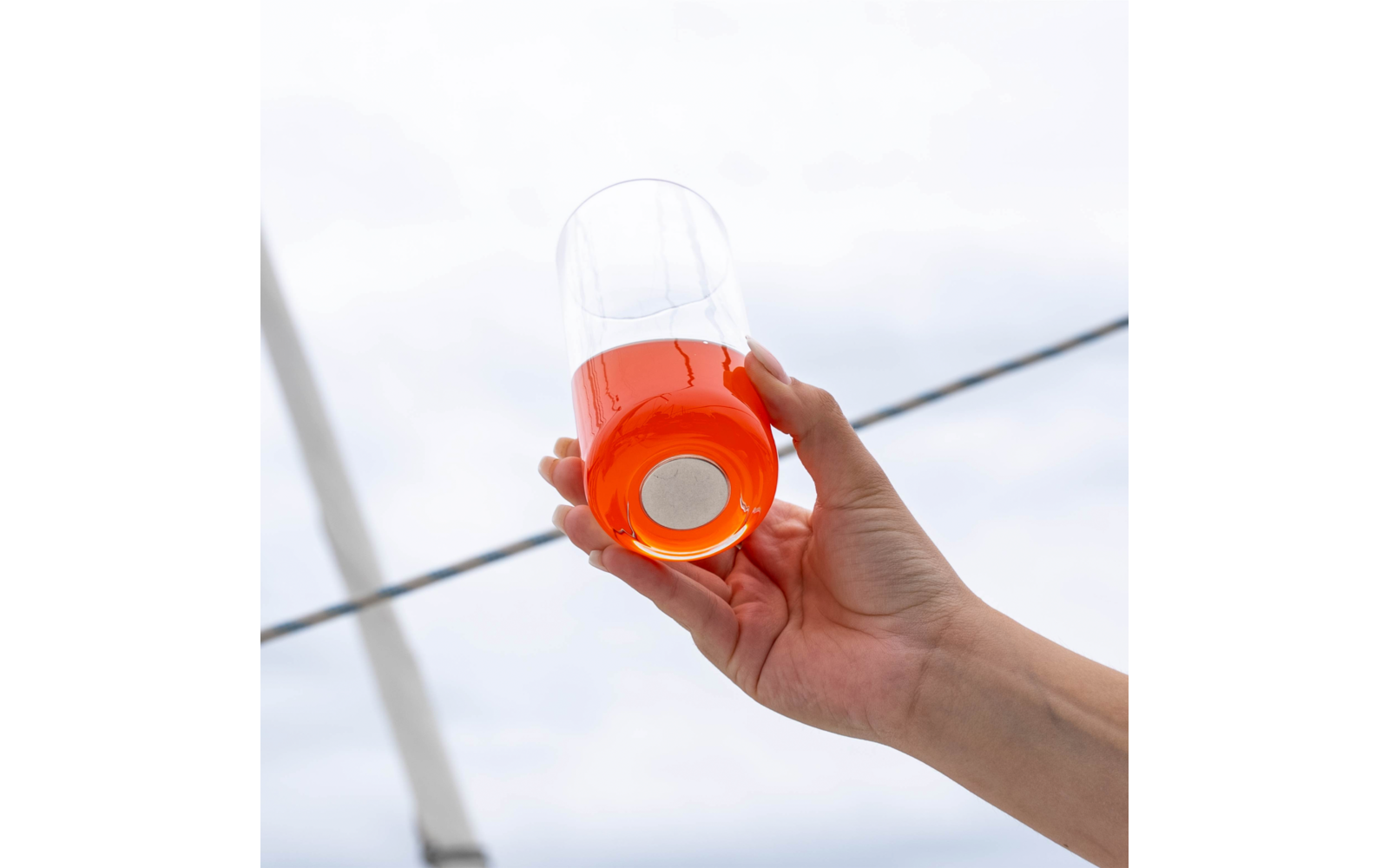 Hand hält ein Glas mit oranger Flüssigkeit vor hellem Himmel