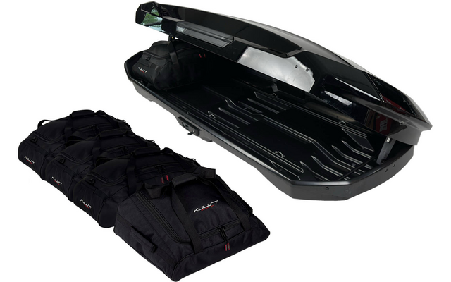 Coffre de toit noir ouvert à côté de quatre sacs de voyage noirs sur fond blanc