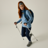 Persona con capelli rossi, fascia grigia, maglione blu, leggings scuri, scarpe da trekking, zaino blu e due bastoncini da trekking su sfondo chiaro