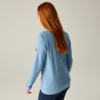 Persona vista da dietro con lunghi capelli rossi, maglia azzurro chiaro a maniche lunghe e pantaloni scuri su sfondo neutro