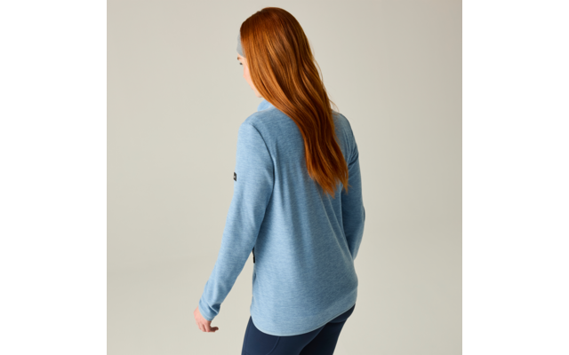 Persona vista da dietro con lunghi capelli rossi, maglia azzurro chiaro a maniche lunghe e pantaloni scuri su sfondo neutro