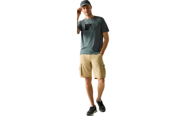 Stehende Person mit Baseballcap, eine Hand an der Krempe, andere Hand in Hosentasche; blaues T‑Shirt mit quadratischem Aufdruck, beige Cargoshorts, schwarze Sneaker