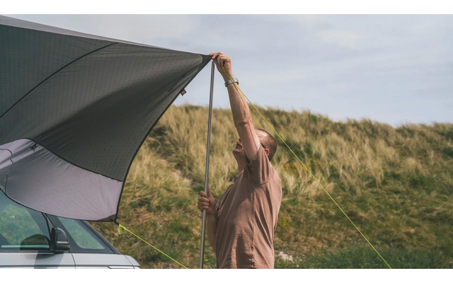Person zieht Plane über ein Zelt in einer grasbewachsenen Dünenlandschaft auf