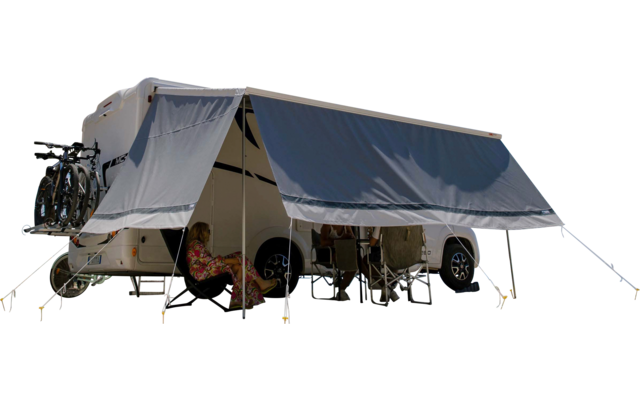 Weißer Wohnwagen mit ausgefahrener Markise, Campingstühle darunter, Bäume links, Meer im Hintergrund, blauer Himmel