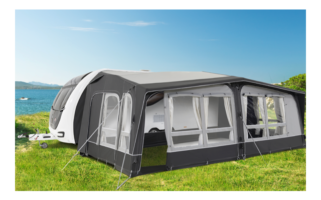 Caravana con toldo adjunto en un césped verde cerca de un lago bajo un cielo despejado