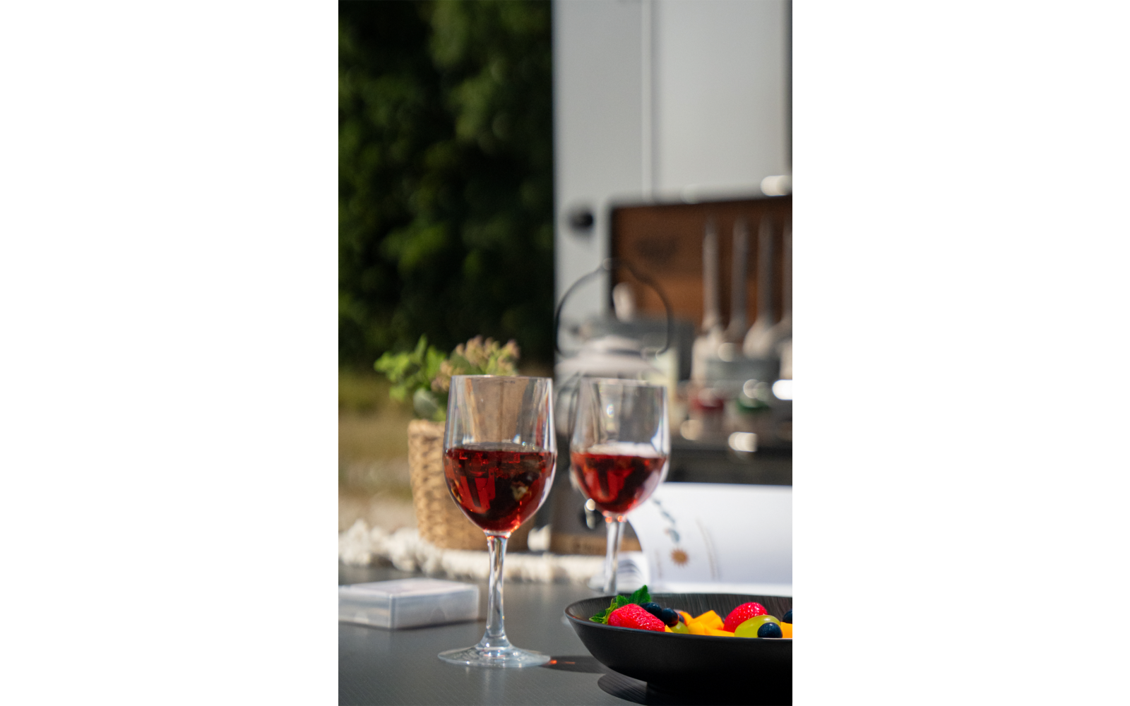 Twee glazen met rode drank op een tafel, houten stoel en groene planten op de achtergrond