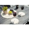 Mesa de madera oscura con dos copas de vino tinto sobre posavasos blancos redondos de macramé; junto a ellas un salvamantel redondo de macramé con una maceta pequeña con planta verde, un cuenco de uvas verdes y oscuras y una botella de vino