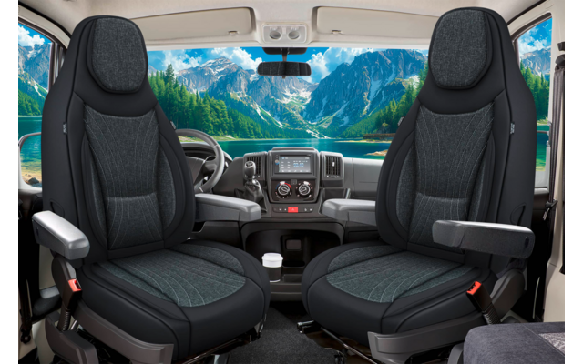 Innenansicht einer Fahrzeugkabine mit zwei dunklen Vordersitzen, Lenkrad, Armaturenbrett und Windschutzscheibe, durch die Berge, einen See und den Himmel sichtbar sind