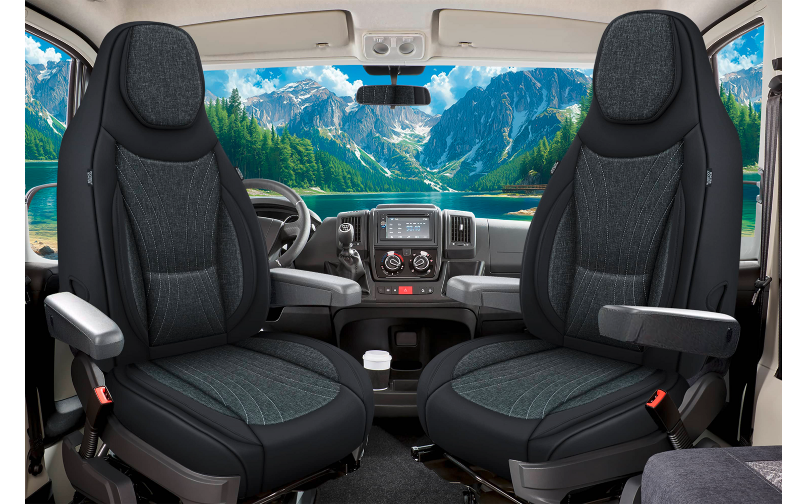 Innenansicht einer Fahrzeugkabine mit zwei dunklen Vordersitzen, Lenkrad, Armaturenbrett und Windschutzscheibe, durch die Berge, einen See und den Himmel sichtbar sind