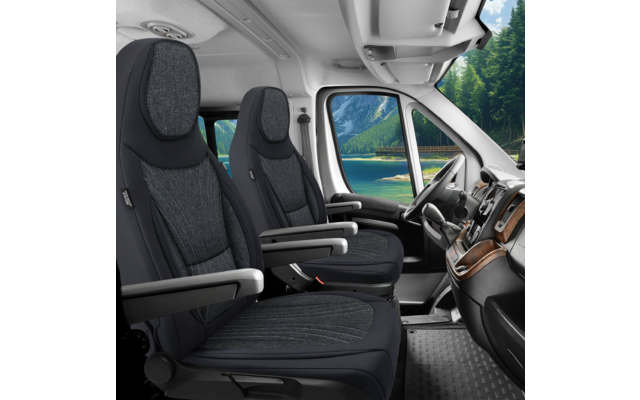 Innenraum eines Vans mit zwei Vordersitzen, Armlehnen, Lenkrad und Armaturenbrett; durch die Seitenscheibe sichtbar: See, Berge und Nadelbäume