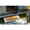 Porte de camping-car ouverte, marche métallique sortie avec paillasson portant l'inscription "welcome", tapis d'extérieur à motifs, herbe et petite table avec plante