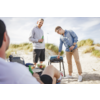 Drei Männer am Strand beim Grillen, einer sitzt, zwei stehen, einer hält ein Bier in der Hand