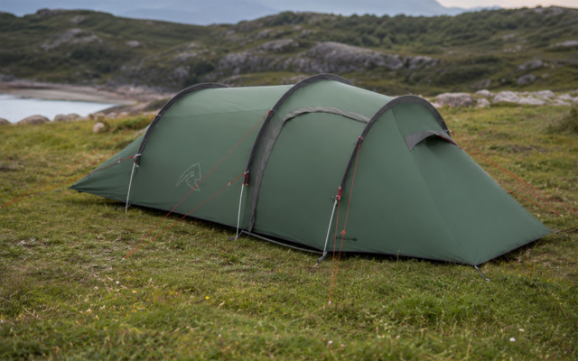 Tente longue verte avec arceaux sur de l'herbe, rochers et eau côtière en arrière-plan
