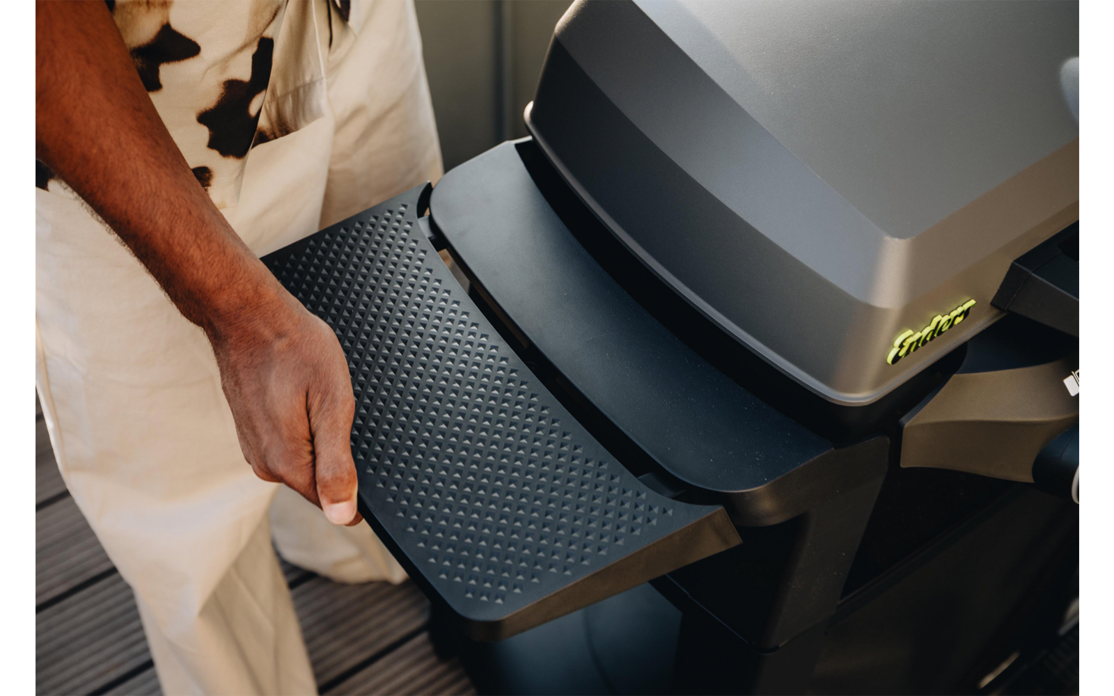 Hand zieht eine strukturierte, ausklappbare Ablage an einem dunkelgrauen Grill