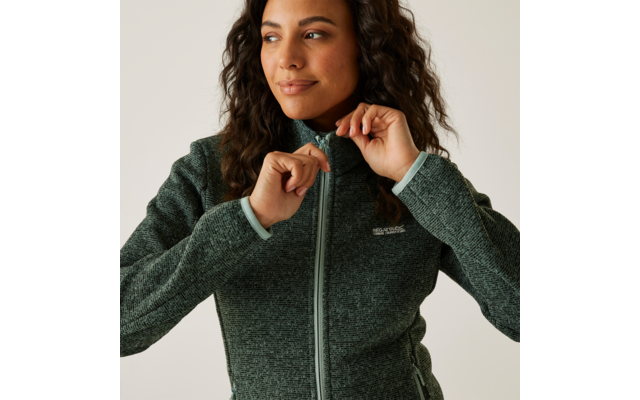 Frau mit dunklen Locken zieht ihren grünen Reißverschluss-Pullover hoch