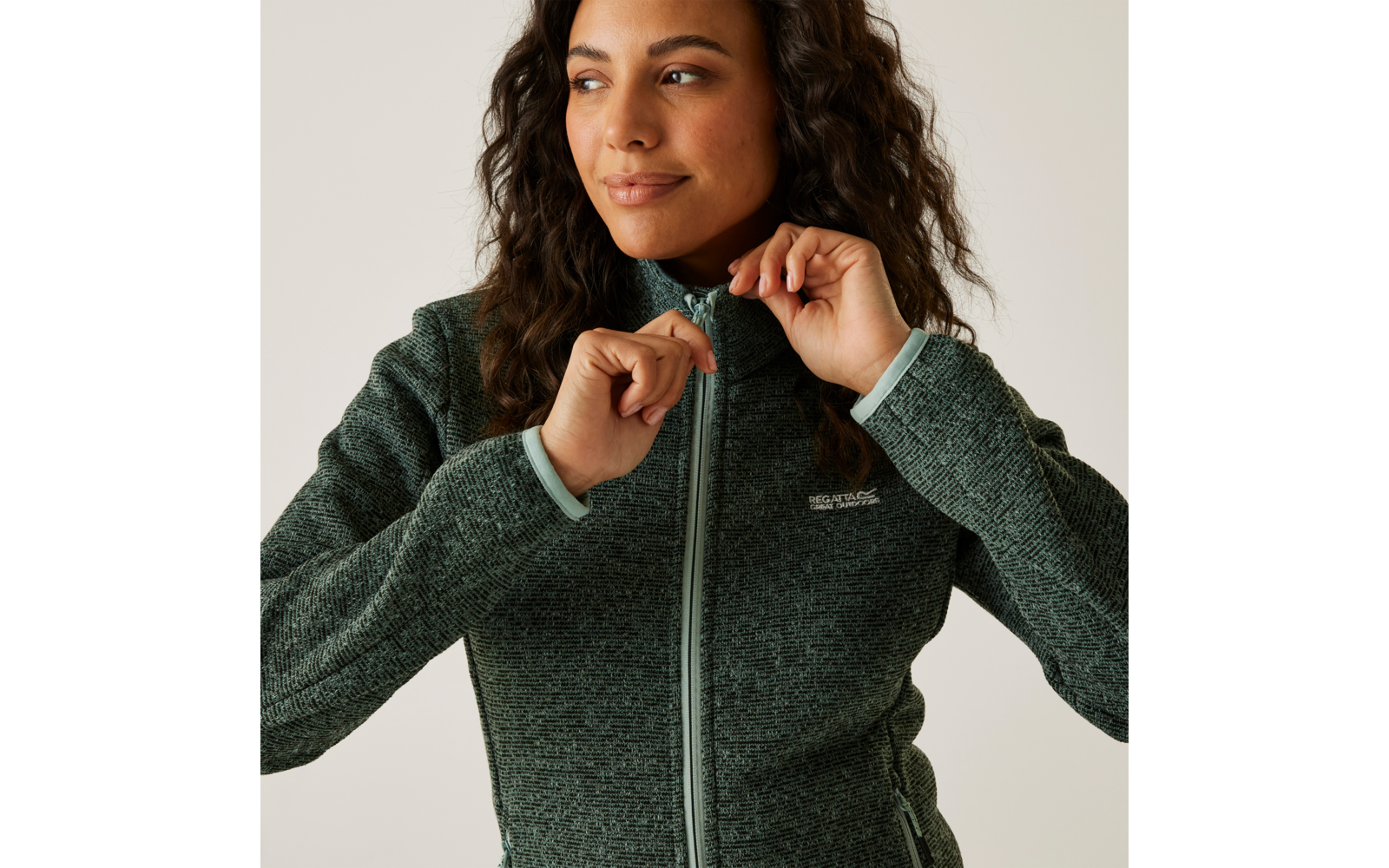 Frau mit dunklen Locken zieht ihren grünen Reißverschluss-Pullover hoch