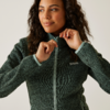 Frau mit dunklen Locken zieht ihren grünen Reißverschluss-Pullover hoch