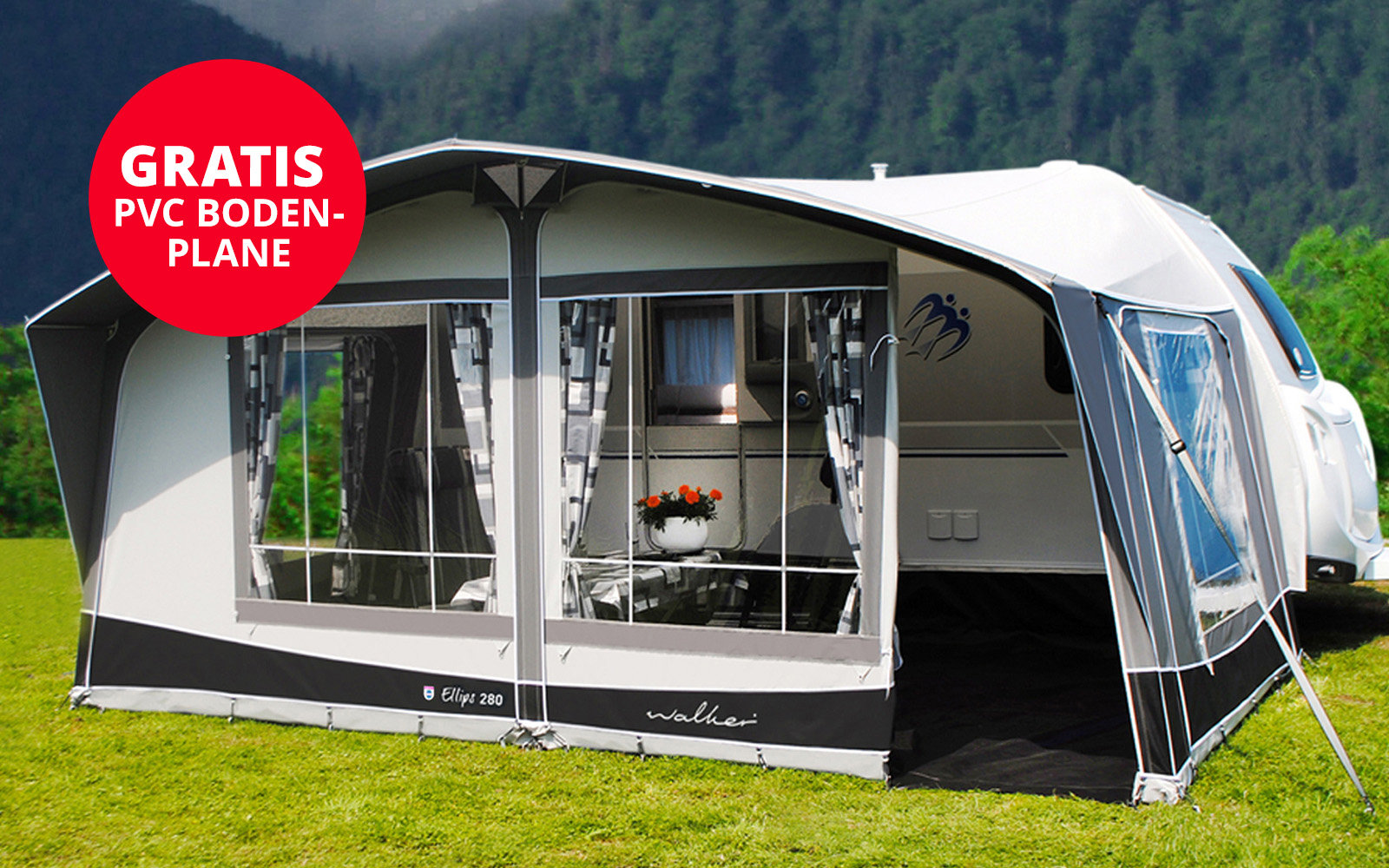 Großes weißes Zelt mit geöffnetem Vorhang auf grünem Rasen, dahinter Berge und Wald