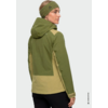 Persona vista di tre quarti di spalle, indossa giacca con cappuccio verde bicolore, fascia per capelli, capelli biondi, pantaloni neri, sfondo grigio chiaro