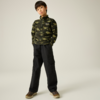 Ein Kind vor hellem einfarbigem Hintergrund, trägt grünen Camouflage‑Pullover mit Kapuze, schwarze Cargohose und braune Sneakers, Hände in den Taschen