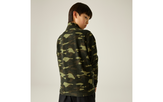 Person von hinten mit kurzem dunklem Haar, trägt grünes Camouflage-Langarmoberteil und dunkle Hose vor hellem Hintergrund