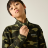 Kind mit kurzem dunklem Haar trägt olivgrünes Camouflage-Fleece, hält den Kragen, heller Hintergrund