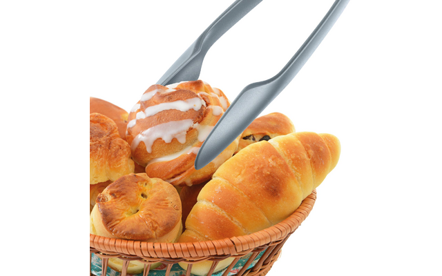 Panier en osier contenant divers petits pains et viennoiseries ; pince en métal tient une viennoiserie avec glaçage blanc ; fond blanc