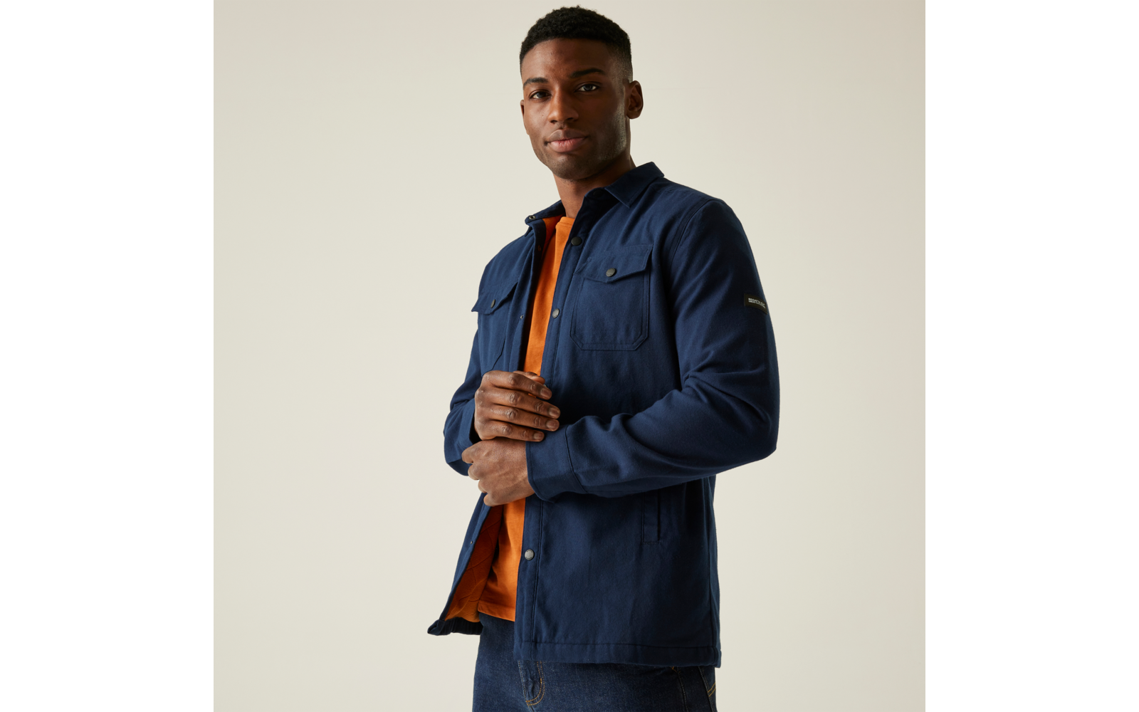 Ein Mann trägt ein dunkles Hemdjacke über einem orangefarbenen Pullover
