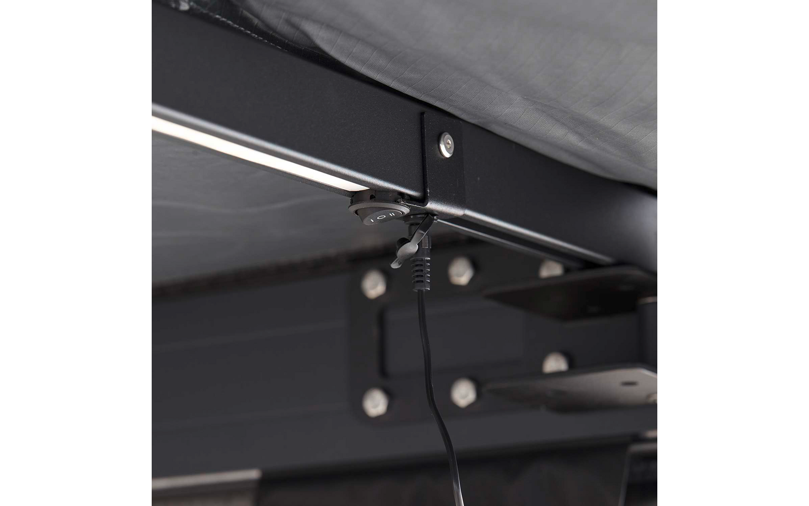 Unterseite eines Metallrahmens mit Matratzenkante, runder Stecker mit Kabel hängt an der Rahmenstange, sichtbare Schrauben