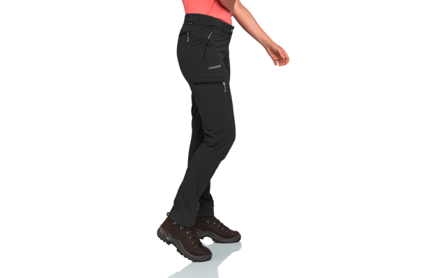 Unterschenkel und Hüfte einer Person in schwarzer langer Hose mit mehreren Reißverschlusstaschen, korallenfarbenes Oberteil sichtbar, braune geschnürte Schuhe