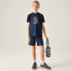 Kind steht vor neutralem Hintergrund, trägt dunkelblaues T‑Shirt mit buntem Motiv, dunkelblaue Shorts, Sportschuhe und hält eine blaue Trinkflasche in einem Netz