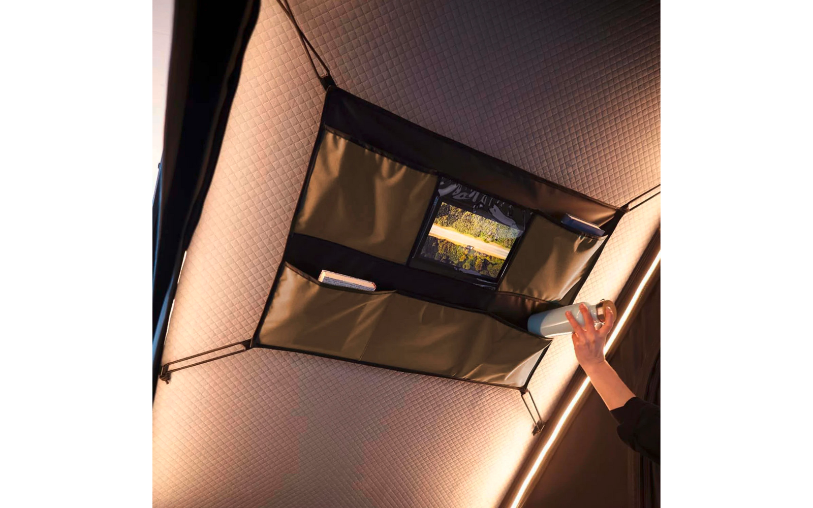 Schwarzer Decken-Organizer mit Taschen an gestepptem Fahrzeughimmel, Tablet in einer Tasche, Papier in einer anderen, rechte Hand hält einen Becher