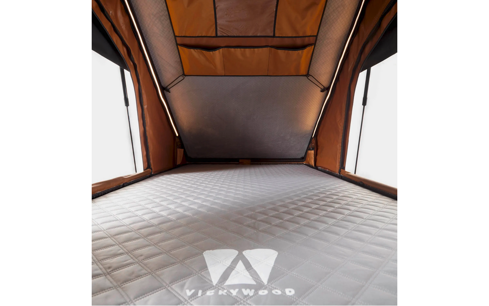 Innenraum eines braunen Zeltes mit gesteppter grauer Matratze, zwei vertikalen Stützstangen, seitlichen Fenstern, Netzfenster im Dach und auf der Matratze sichtbarem Logo "VICKYWOOD"