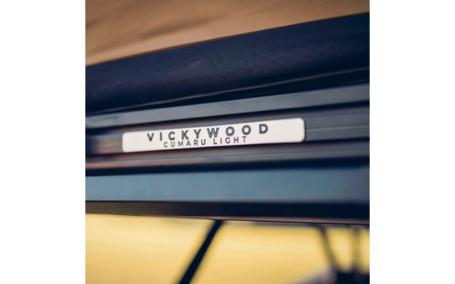 Nahaufnahme eines rechteckigen Metalllabels mit der Aufschrift VICKYWOOD CUMARU LIGHT auf einer dunklen Oberfläche; unscharfer gelblich-brauner Hintergrund