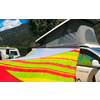 Camper blanc avec toit relevé et auvent rayé jaune-rouge-vert vif fixé dessus, montagnes, arbres et ciel bleu en arrière-plan