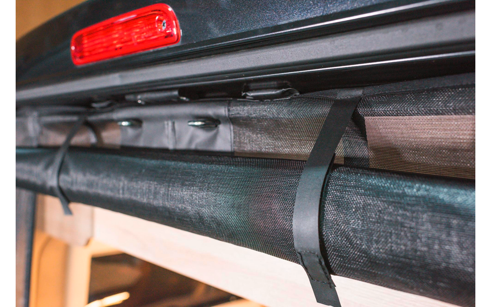 Nahaufnahme eines schwarzen Zurrgurts an einem grauen Gepäckträger eines Fahrzeugs