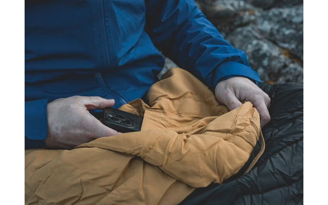 Een persoon houdt een gele jas en een smartphone vast, zittend op donkere rotsen