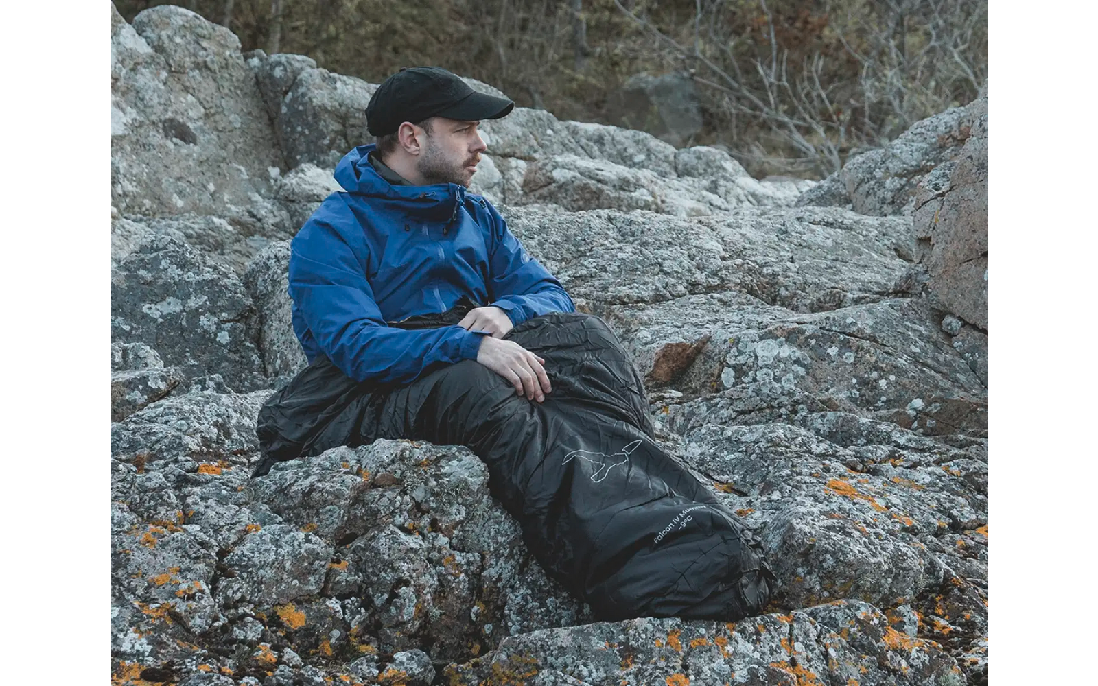 Man in een blauwe jas en zwarte broek zittend op rotsen met bladeren