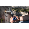 Metallwasserhahn an einer Außenwand, eine Hand hält einen blauen Schlauchanschluss, Unterarm mit Armbanduhr, Boden und Schatten im Hintergrund