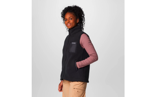 Frau trägt schwarzen ärmellosen Fleecepullover über rosa langärmligem Shirt vor grauem Hintergrund
