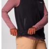 Person zieht einen schwarzen Reißverschluss an einer schwarzen Weste hoch, trägt rosa langärmliges Shirt und beige Hose
